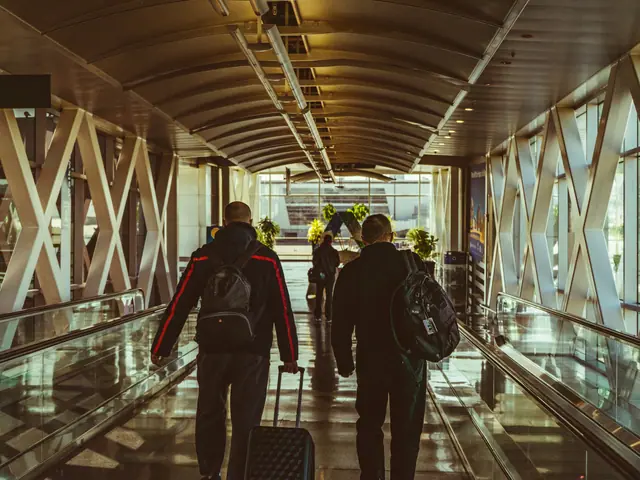 Dois viajantes de mochila e mala andando numa passarela de aeroporto